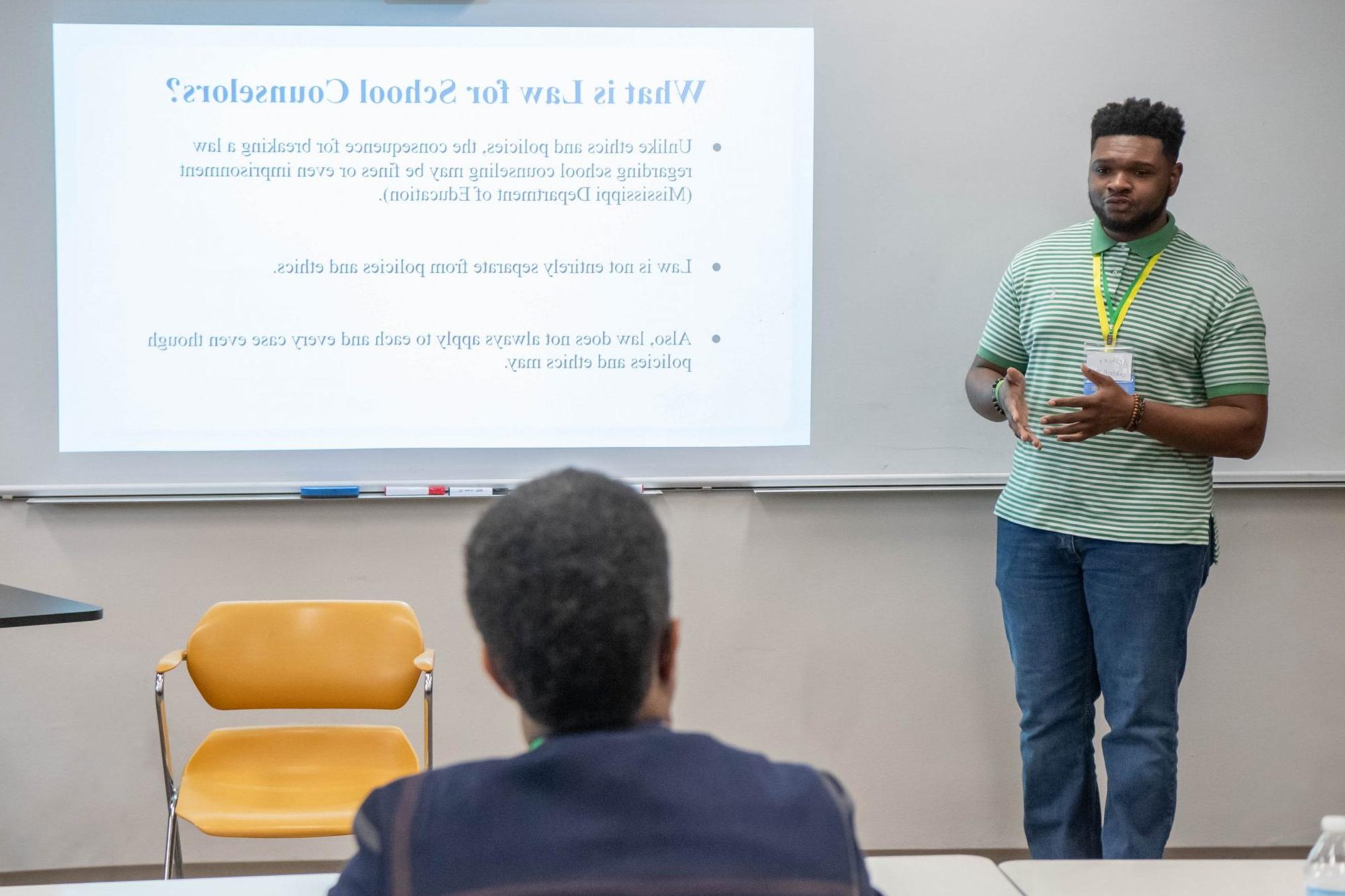 Student standing next to display of PowerPoint presentation, discussing information while a person listens.